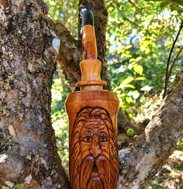 Pilão de madeira entalhado com rosto de ancião barbudo, apoiado em árvore